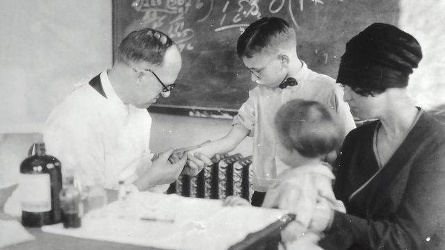A black and white image of a doctor testing a child. 