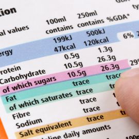 Person's finger tracing down a nutrition label on food packaging. 