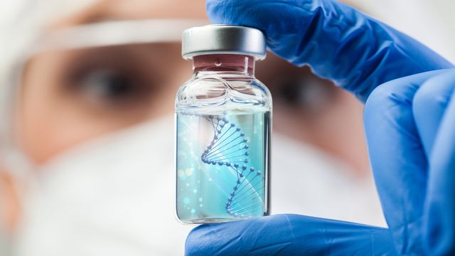 A researcher holds up a vial of liquid containing a strand of DNA. 