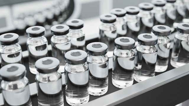 Clear glass vials filled with a colourless liquid sit on a conveyor belt. 