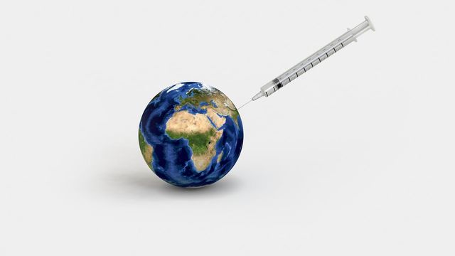 Oversized syringe containing a vaccine being injected into the world. 